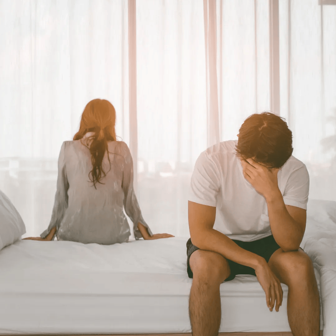 A couple sits on a bed facing away from each other; the scene suggests a possible marital crisis.