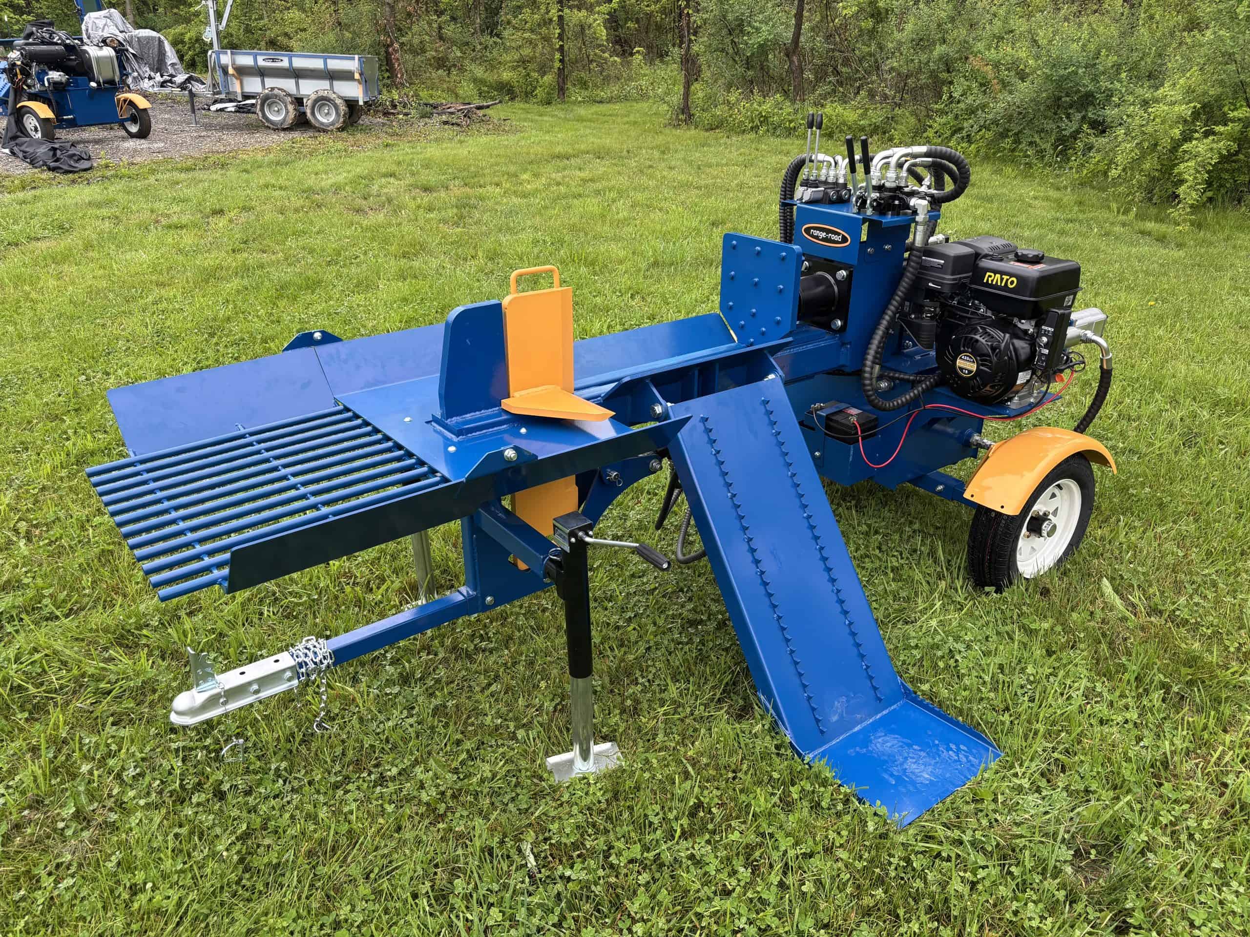 Heavy-duty blue log splitter on grassy field with trees in background.
