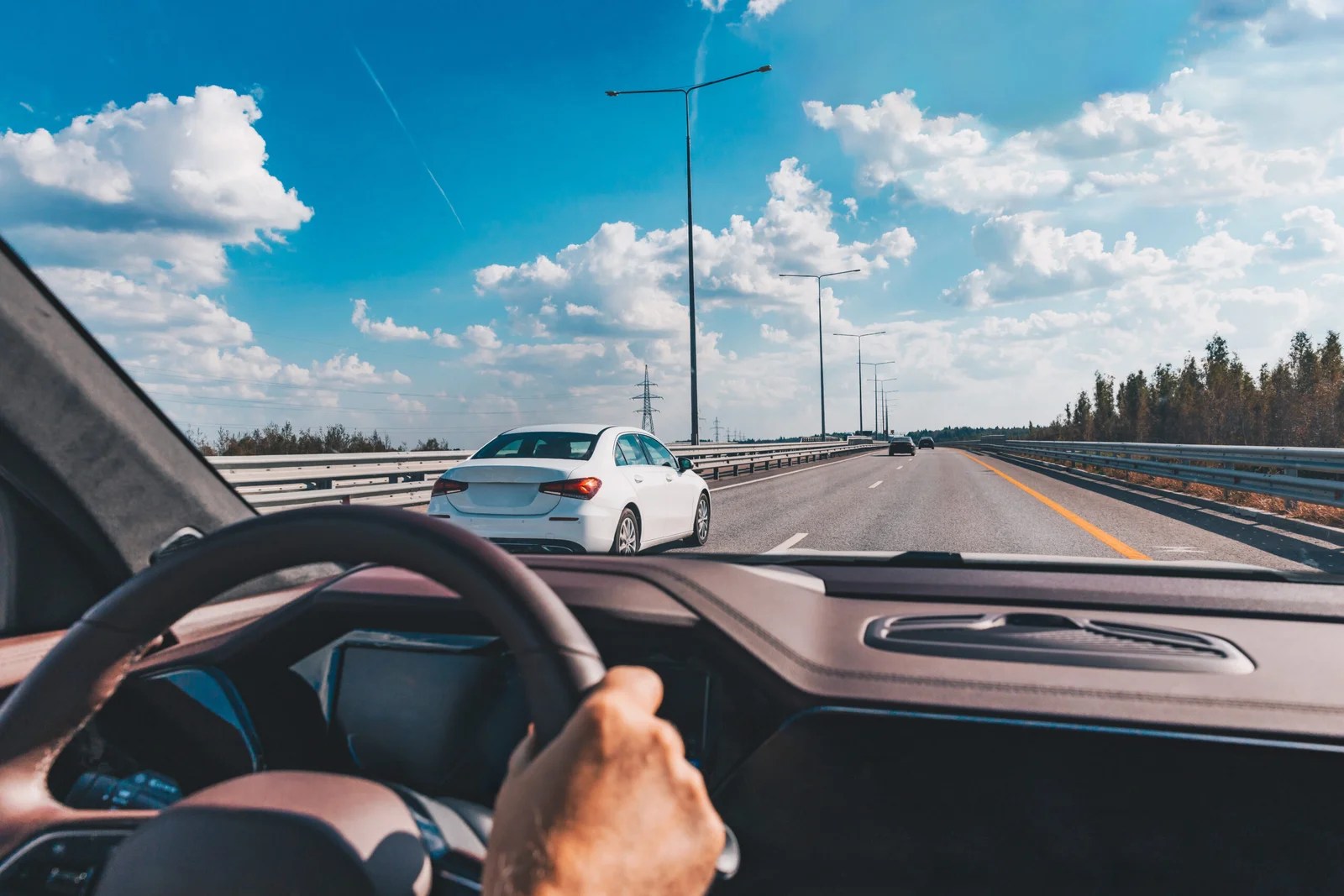 Man driving modern car from rear view on the highway. Hands on t