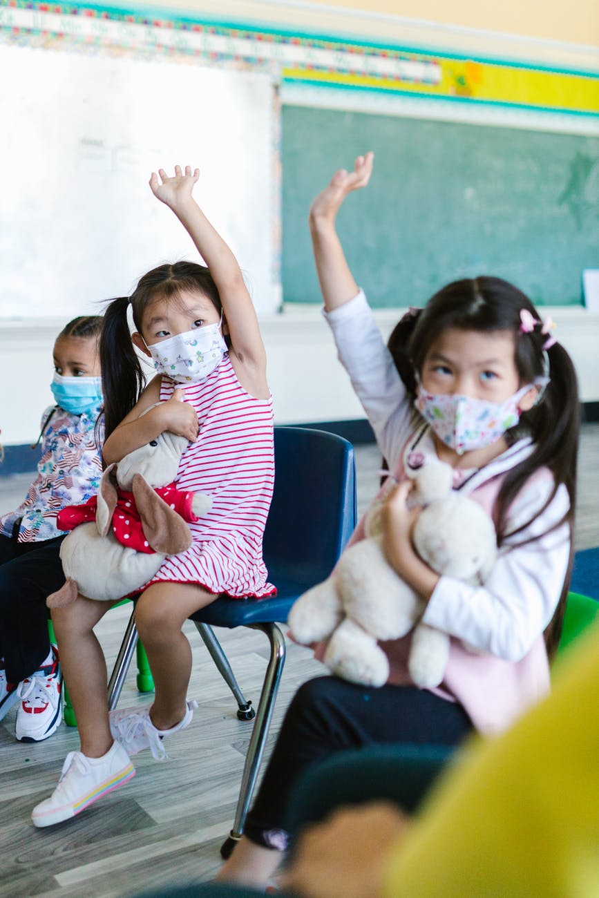 girls wearing facemasks raising hands
