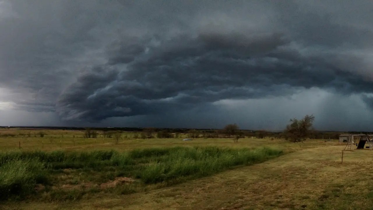 Dark storm clouds forming over a rural landscape, signaling an approaching tornado.