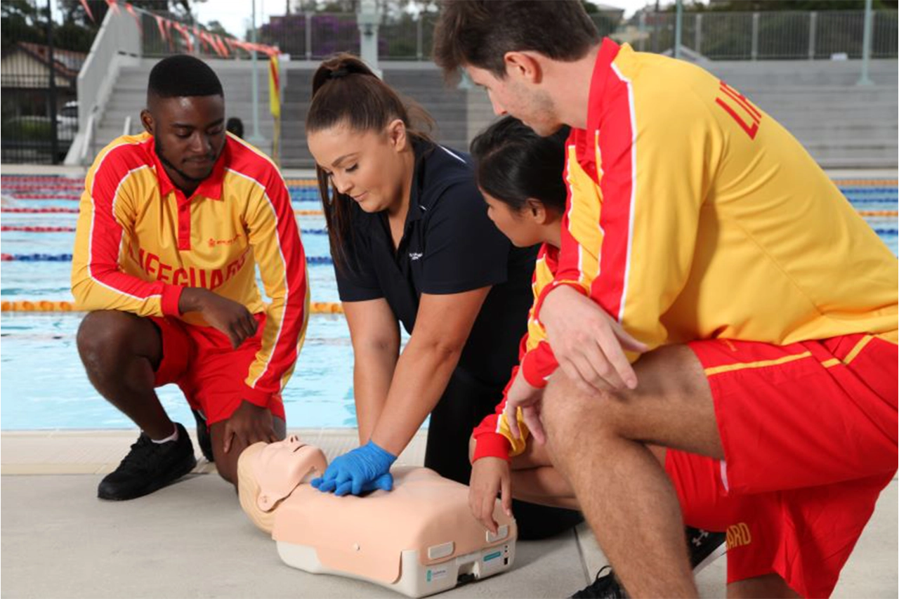 Lifeguards watching a female trainer apply CPR to a dummy