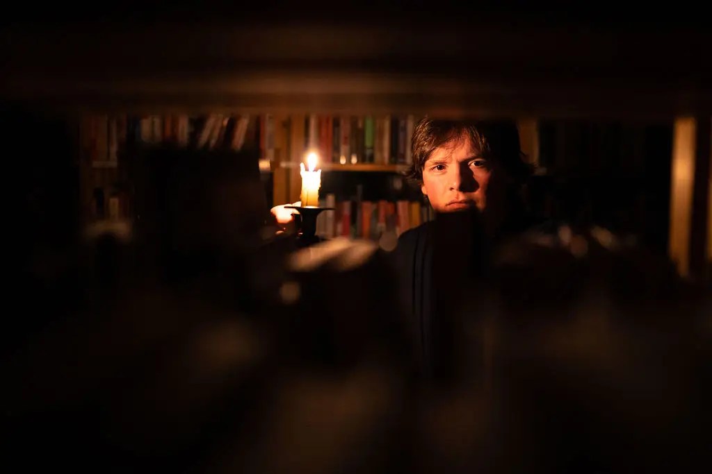 An adventurer exploring a library by candlelight.