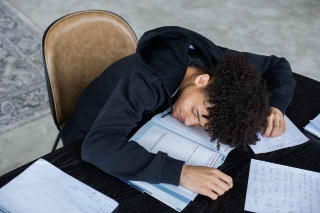 tired black man lying on opened book and homework papers