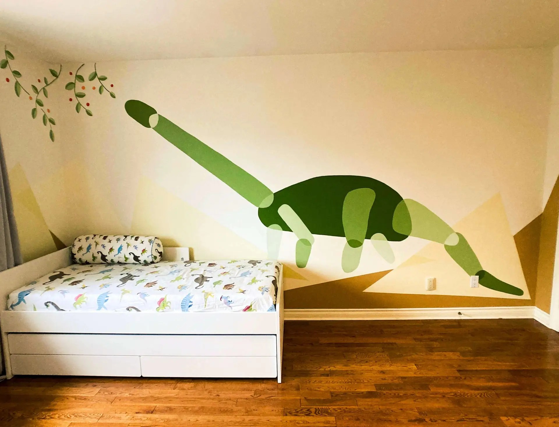 Kid's room showing a IKEA pullout bed with dinosaur patterned bed sheets and a mural of a diplodocus reaching high for leaves and fruits depicted coming from the ceiling.