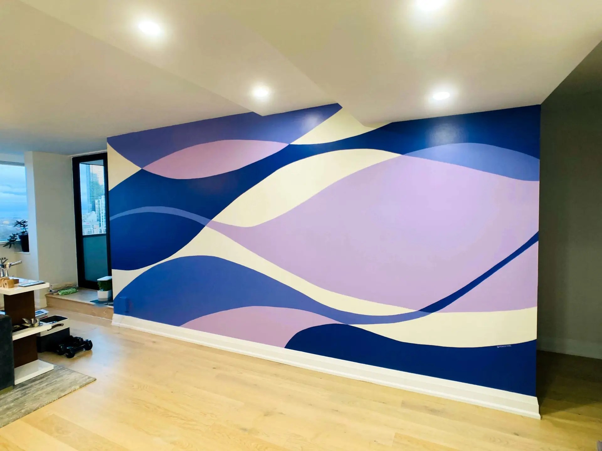 Room with a wall mural with waves in different shades of purple over an off-white background.