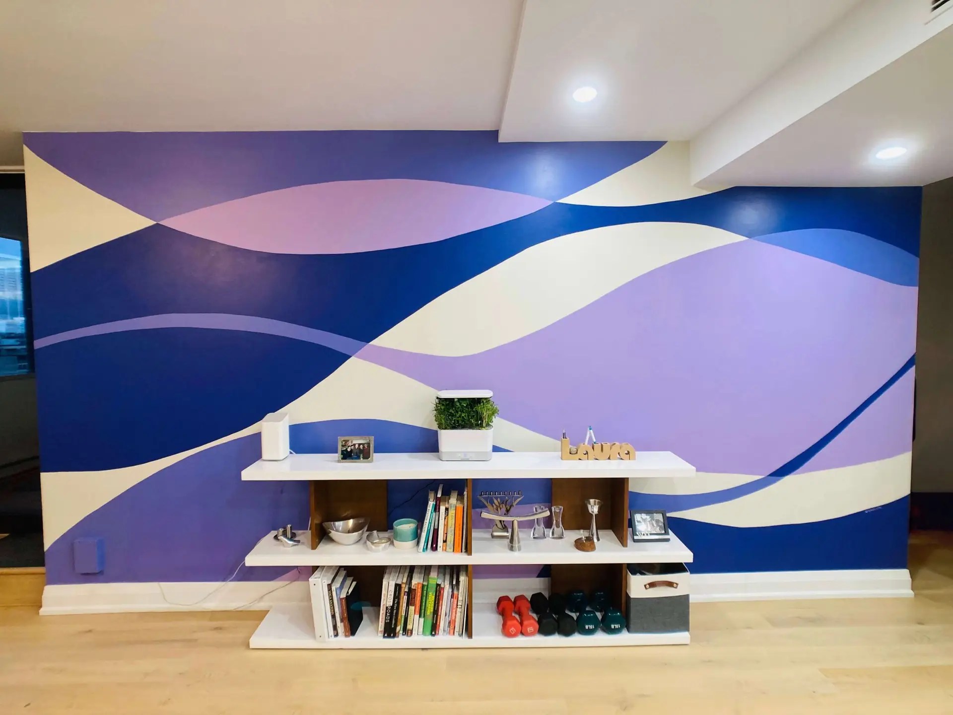 Room with a wall mural with waves in different shades of purple over an off-white background.