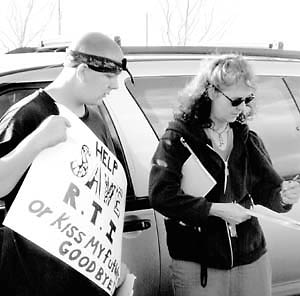 Luke Roach, a student at the Regional Technical Institute, watches Laura Rund sign a petition supporting RTI.
