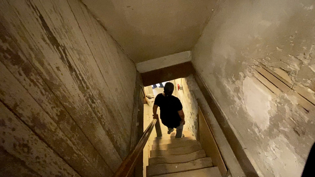 A person descends a dimly lit set of stairs into a basement.