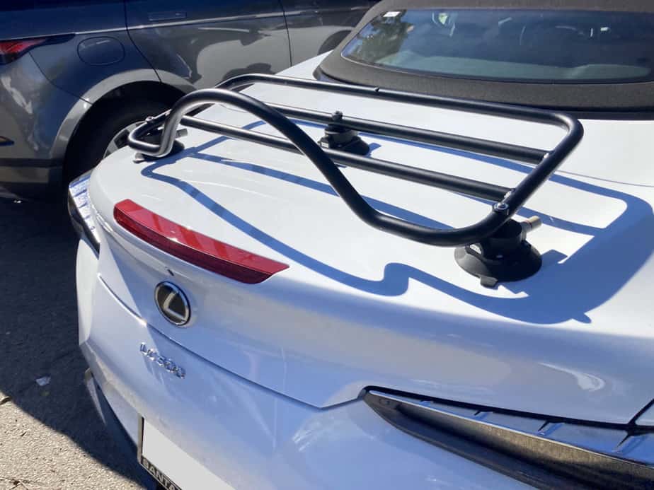 white Lexus LC 500 convertible with a tan hood and a revo-rack pa luggage rack fitted to the trunk photographed from the rear on a car lot in LA