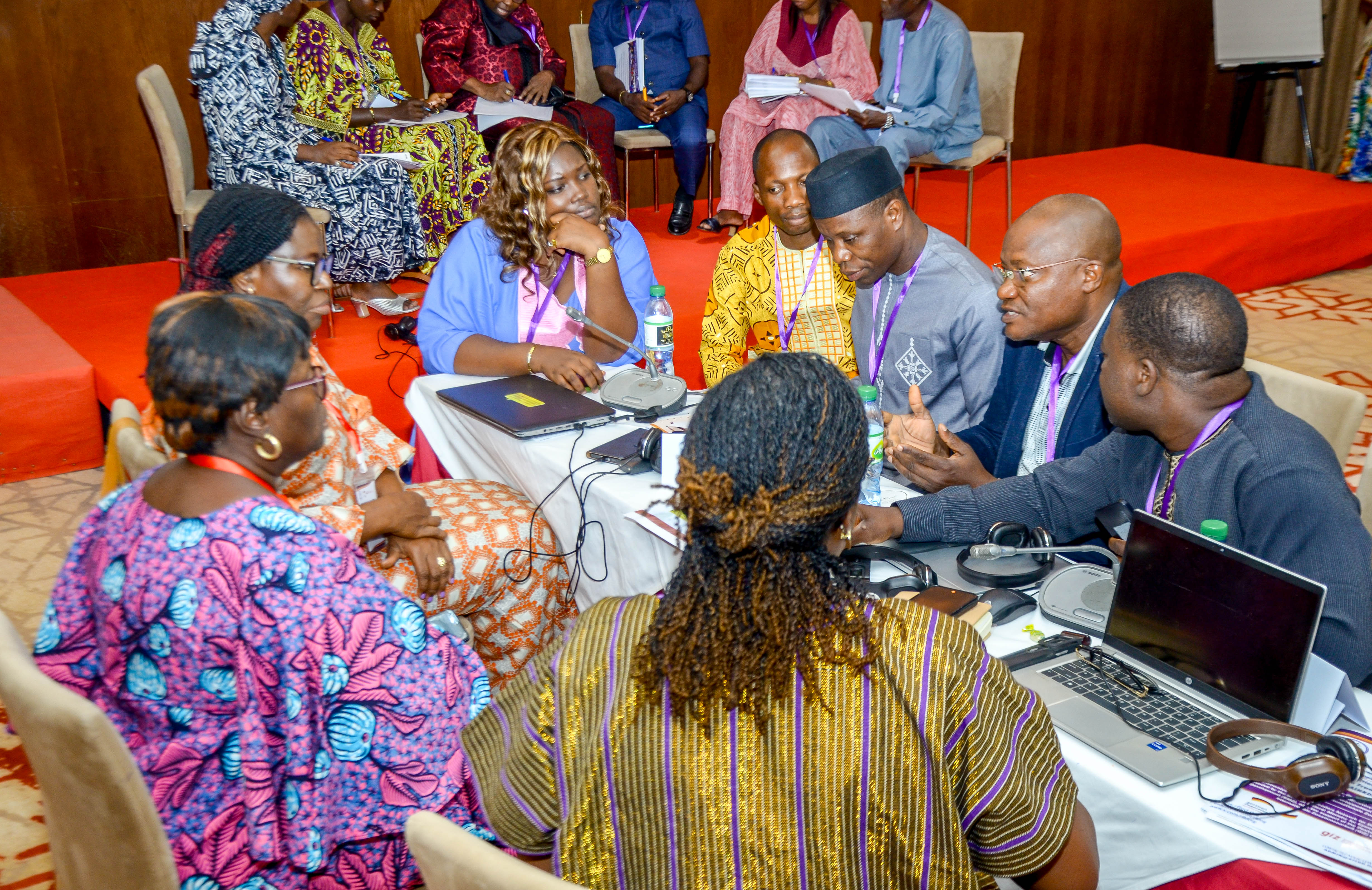 A group of people engaged in a discussion around a table with laptops and communication equipment during a workshop or meeting.