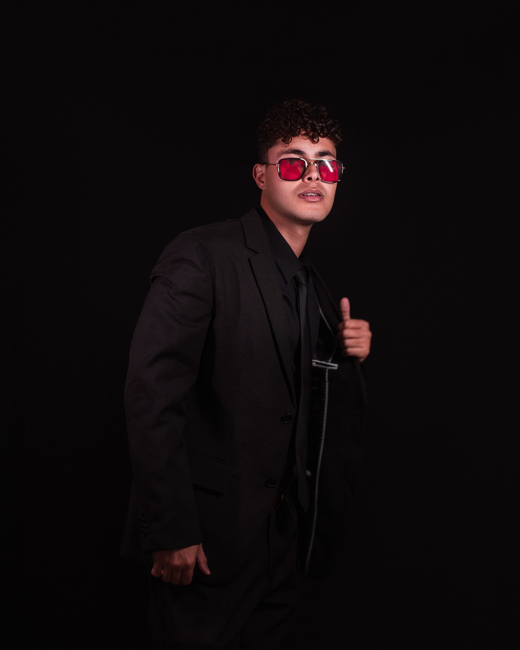 Editorial portrait featuring a dark suit and red eyewear.