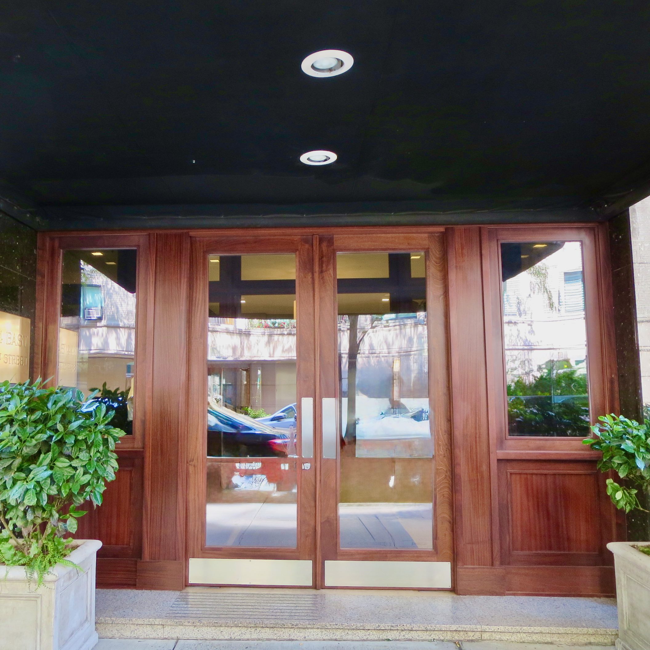 A beautifully designed wooden entryway with glass panels, flanked by planters. The doors are framed with a rich wood finish, showcasing a blend of modern aesthetics and durability.