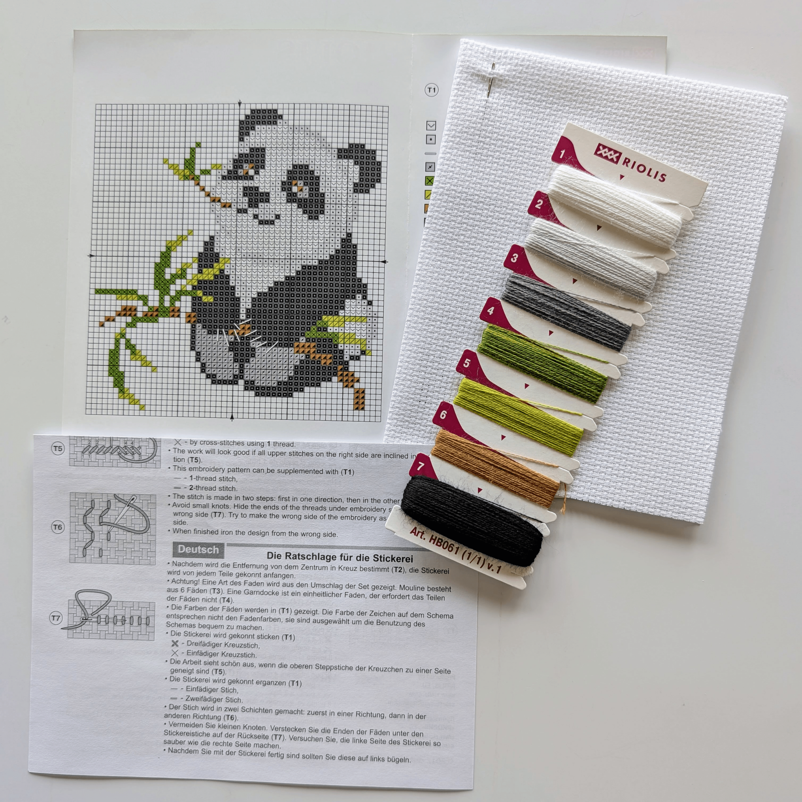 Cross-stitch of a cute panda holding bamboo leaves, stitched in black, white, and green, framed in red.