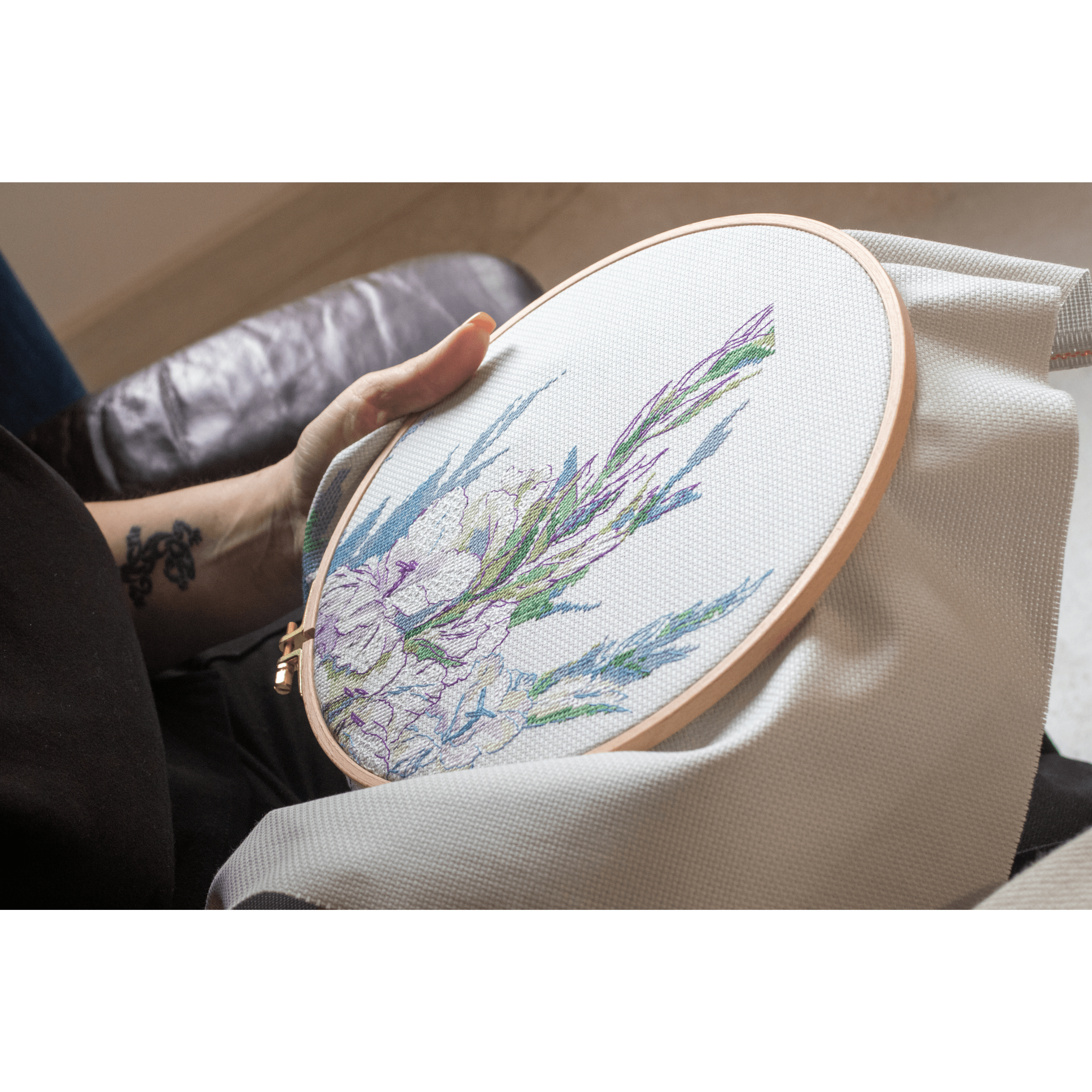 A delicate blackwork embroidery design of white gladiolus flowers with green leaves, stitched against a softly patterned background.