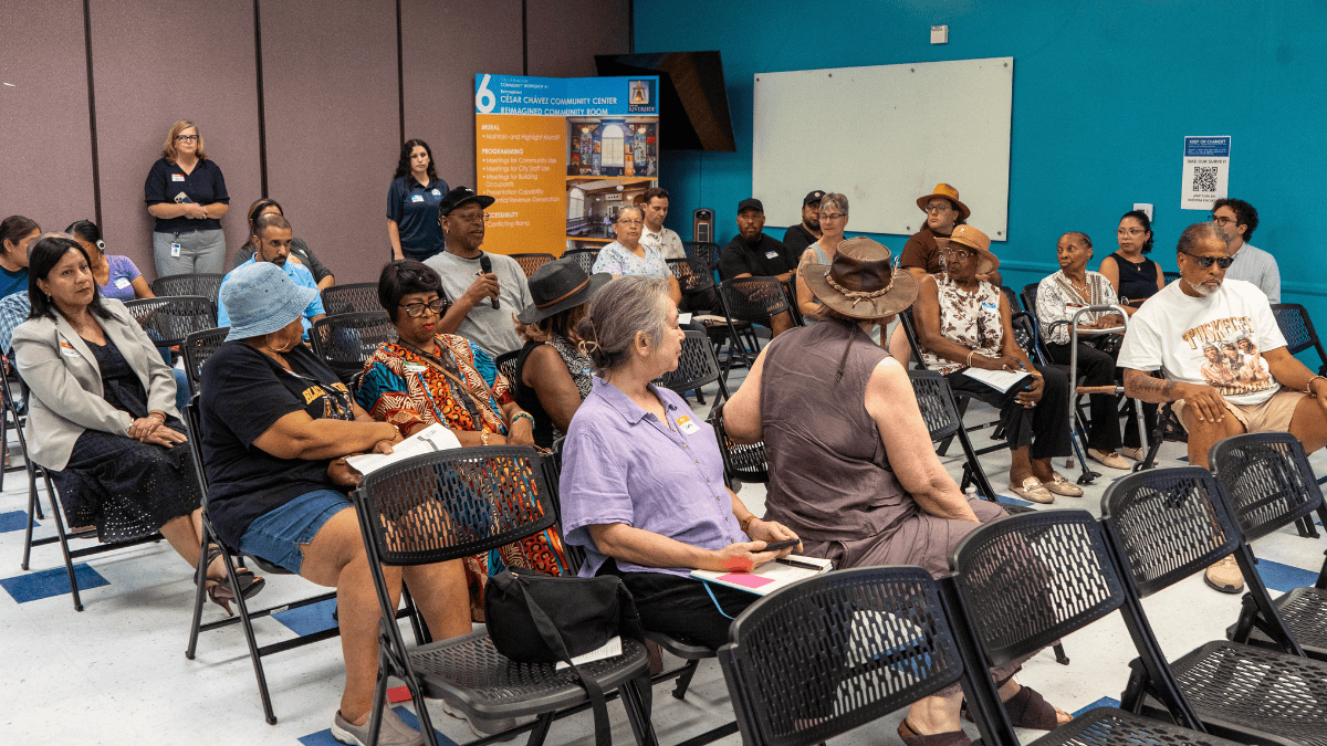 A group of people sitting in chairs listening as one person with a microphone speaks.