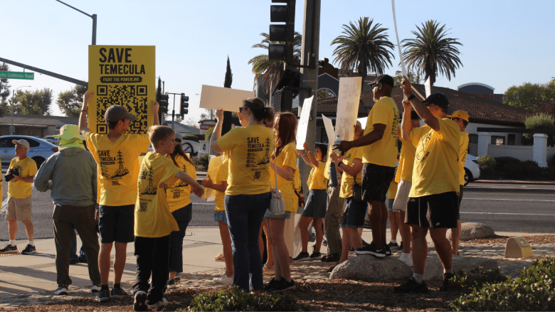A group of people in yellow shirts holding large signs