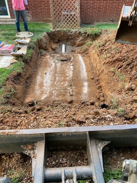 Deep rectangular pit excavated in soil with a level gravel bed prepared for concrete septic tank placement.