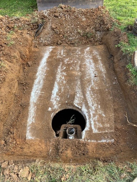 Overhead view of an excavated septic system pit prepared for tank vault dropping and main sewer pipe inlet connection.