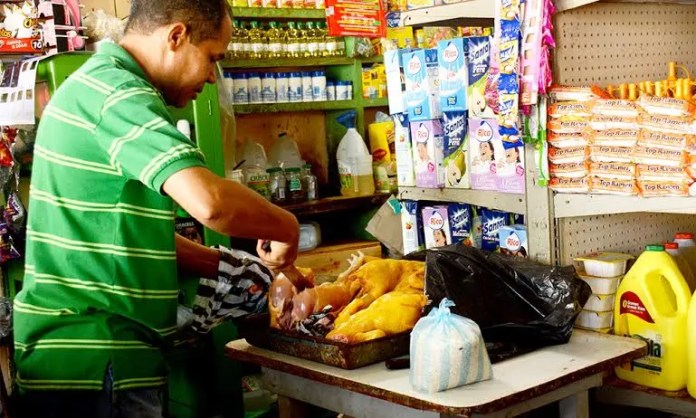 Foto de un comerciante cortando pollo en un colmado.