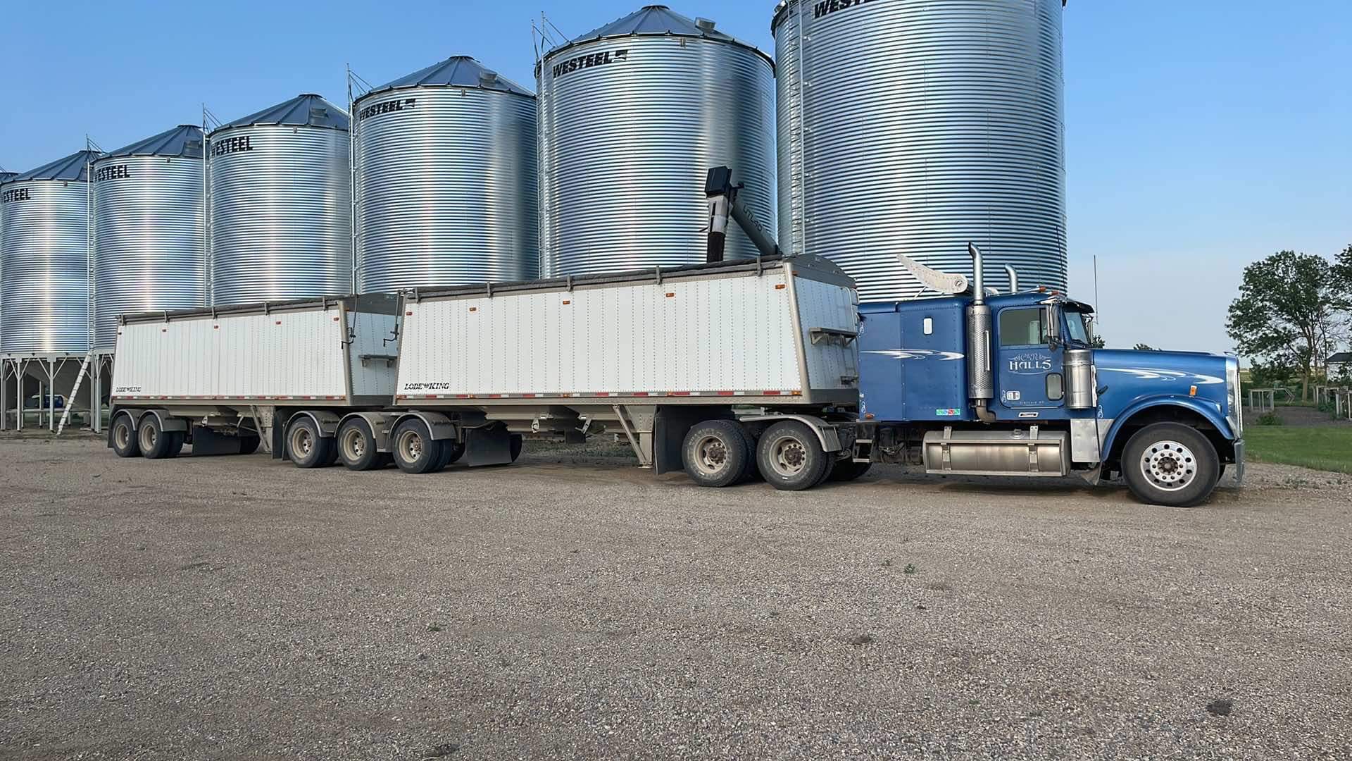 photo of a super b semi being loaded with canola in front of steel grain bins