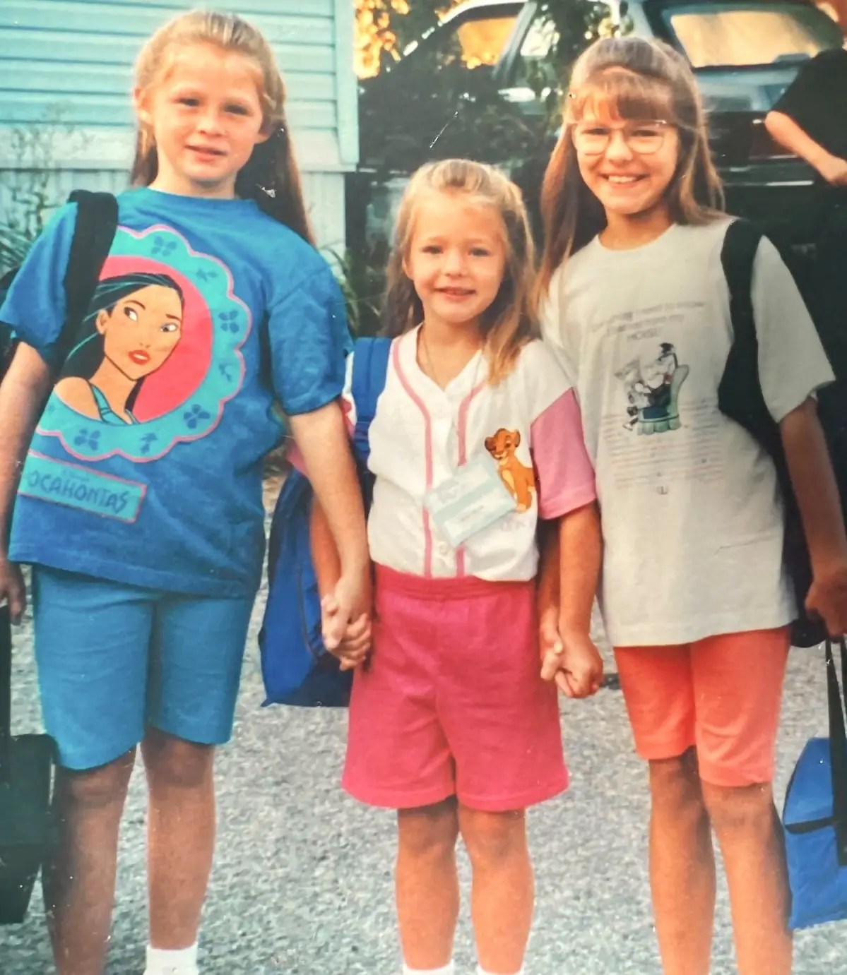 Three sisters smiling with backpacks in a childhood photo