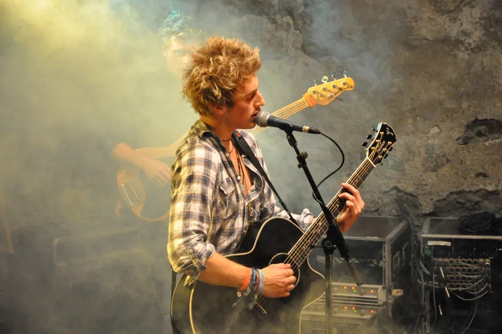 Blonder Singer Songwriter spielt schwarze Gitarre und singt