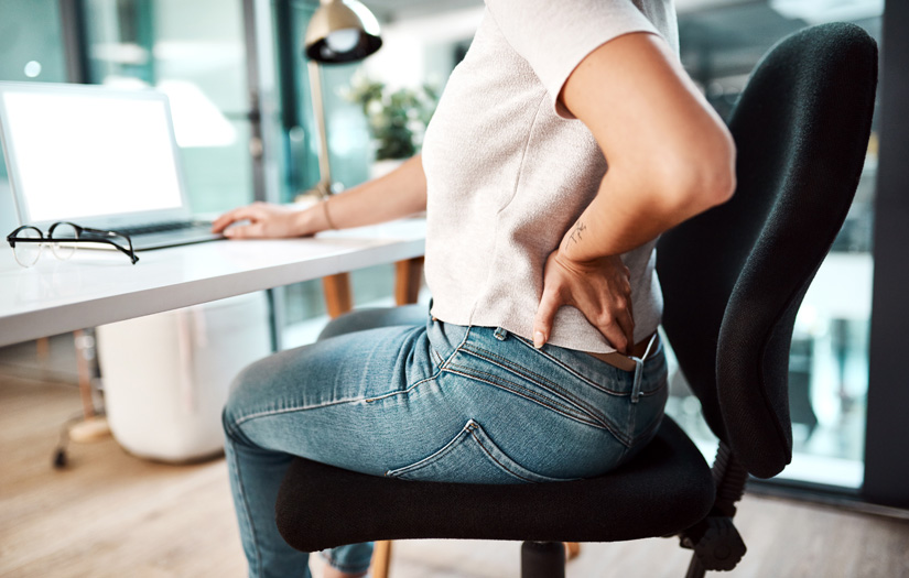 Woman sitting at an office desk holding her back from pain