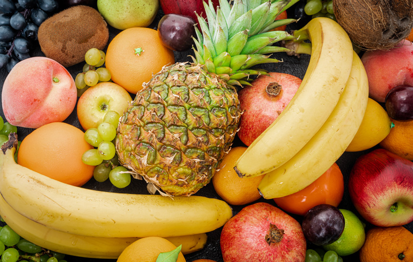 Assortment of fruit with pineapple, bananas, blueberries, apples, peaches, oranges, pomegranate, grapes, kiwi, coconut, raspberries, avocado