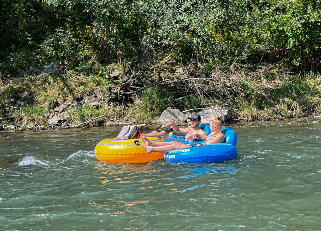 A man in an orange tube and a woman in a blue tube float closely together in flowing river water.