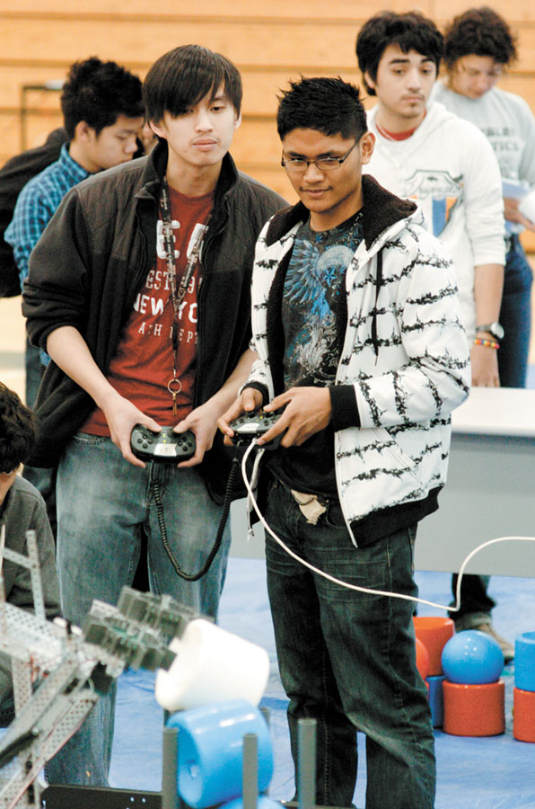 Billy Liu, left, and Lord Nicklyn Labiano stand on the sidelines and remotely “drive” their robot to pick up and place items, part of the competition process.