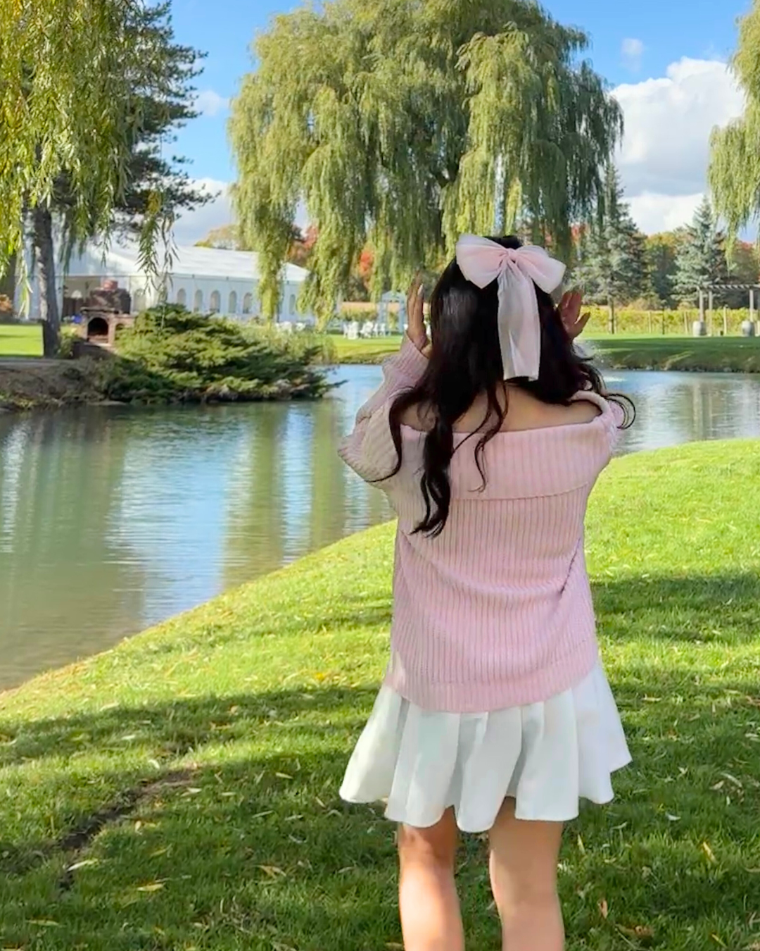 wearing a pink ribbon hair clip and cozy fall outfit, posing by the pond at Willow Springs Winery near Toronto. Scenic fall aesthetic with soft Pinterest-style countryside vibes