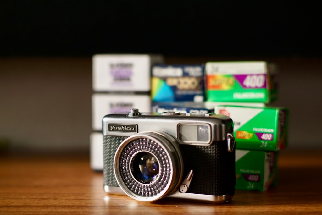 A vintage Yashica camera in focus with several rolls of film stacked in the background, showcasing a nostalgic photography setup.