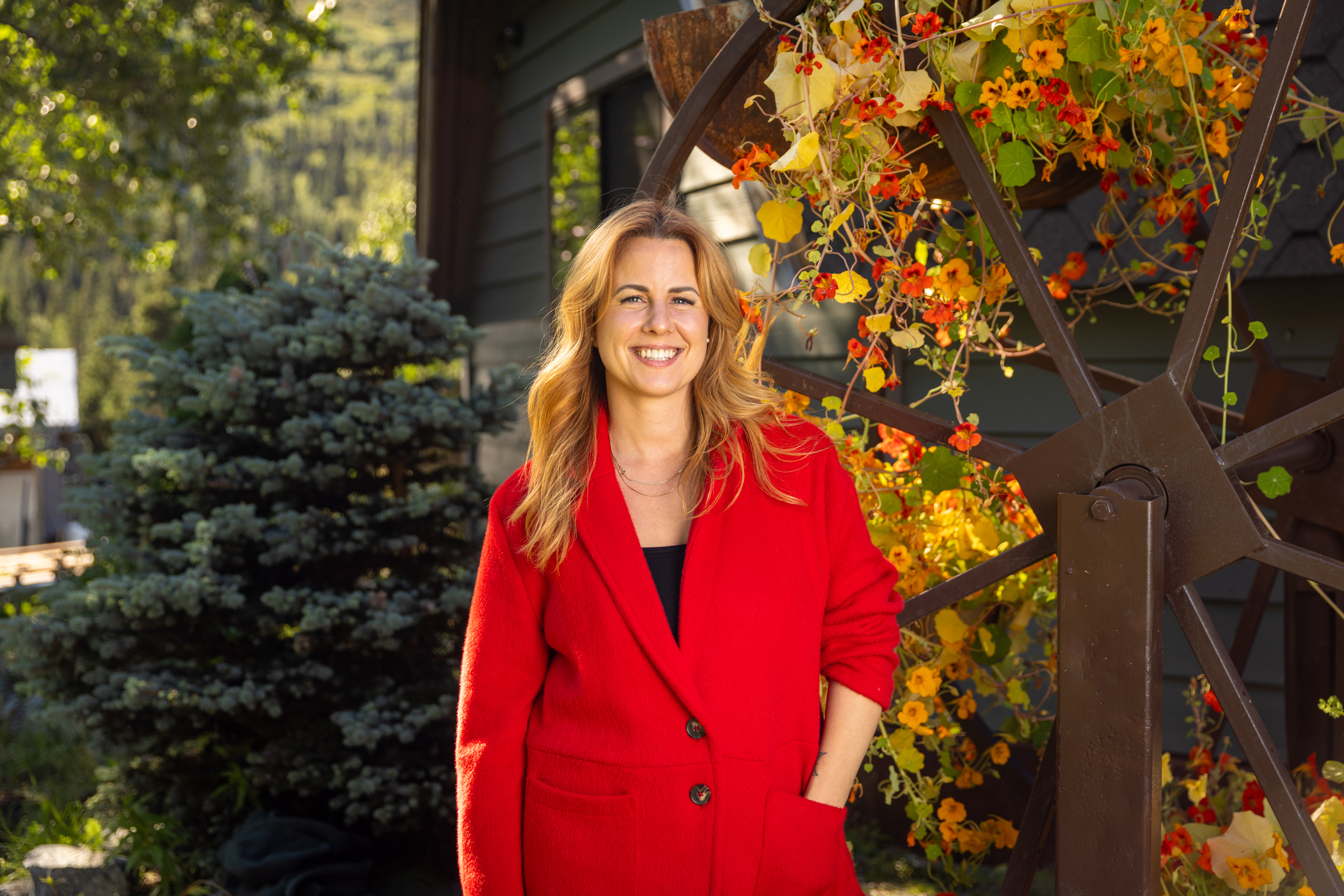 Ruby Jones in a red blazer standing by a flowering trellis outside a home