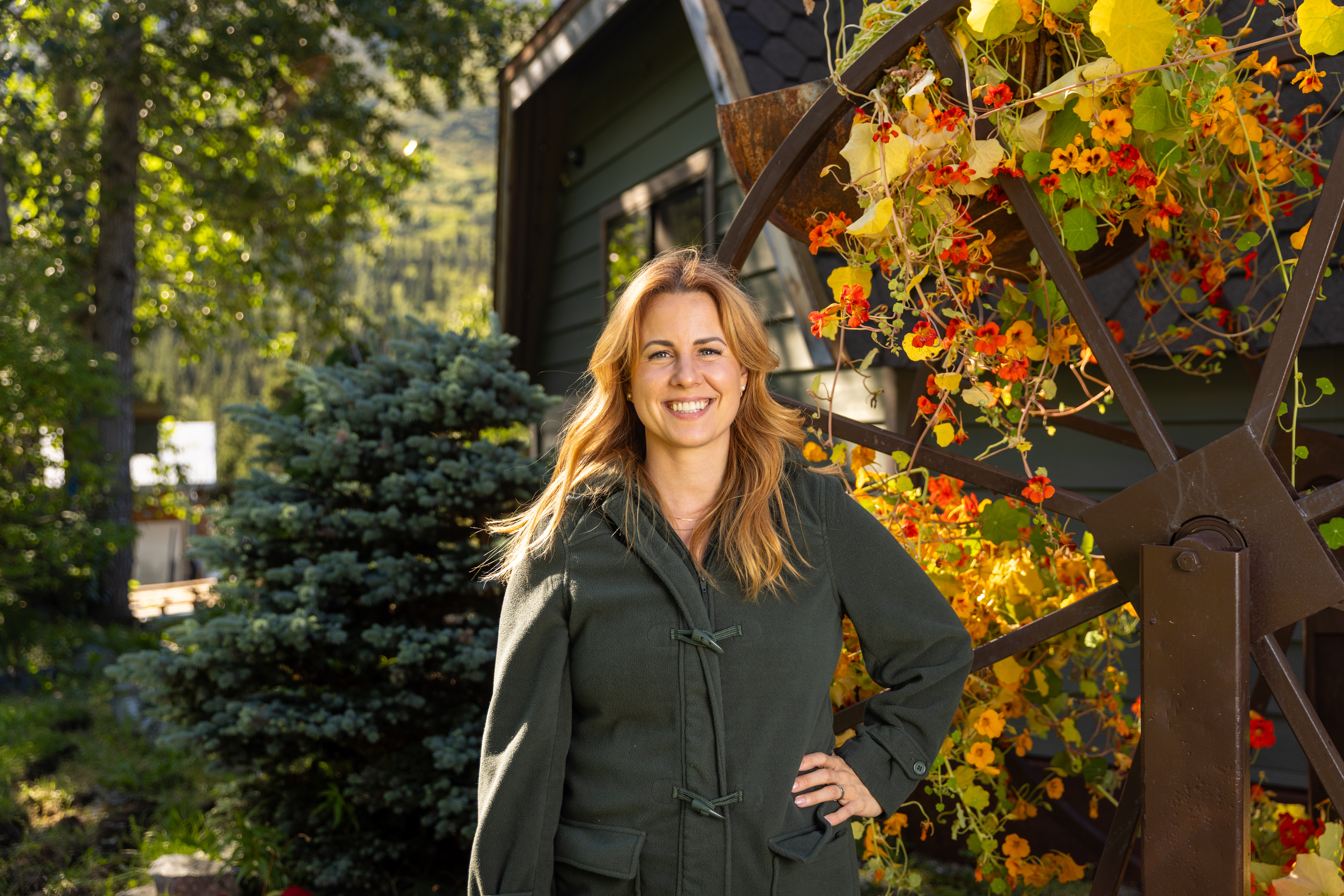Ruby Jones in a green jacket standing by a flowering trellis