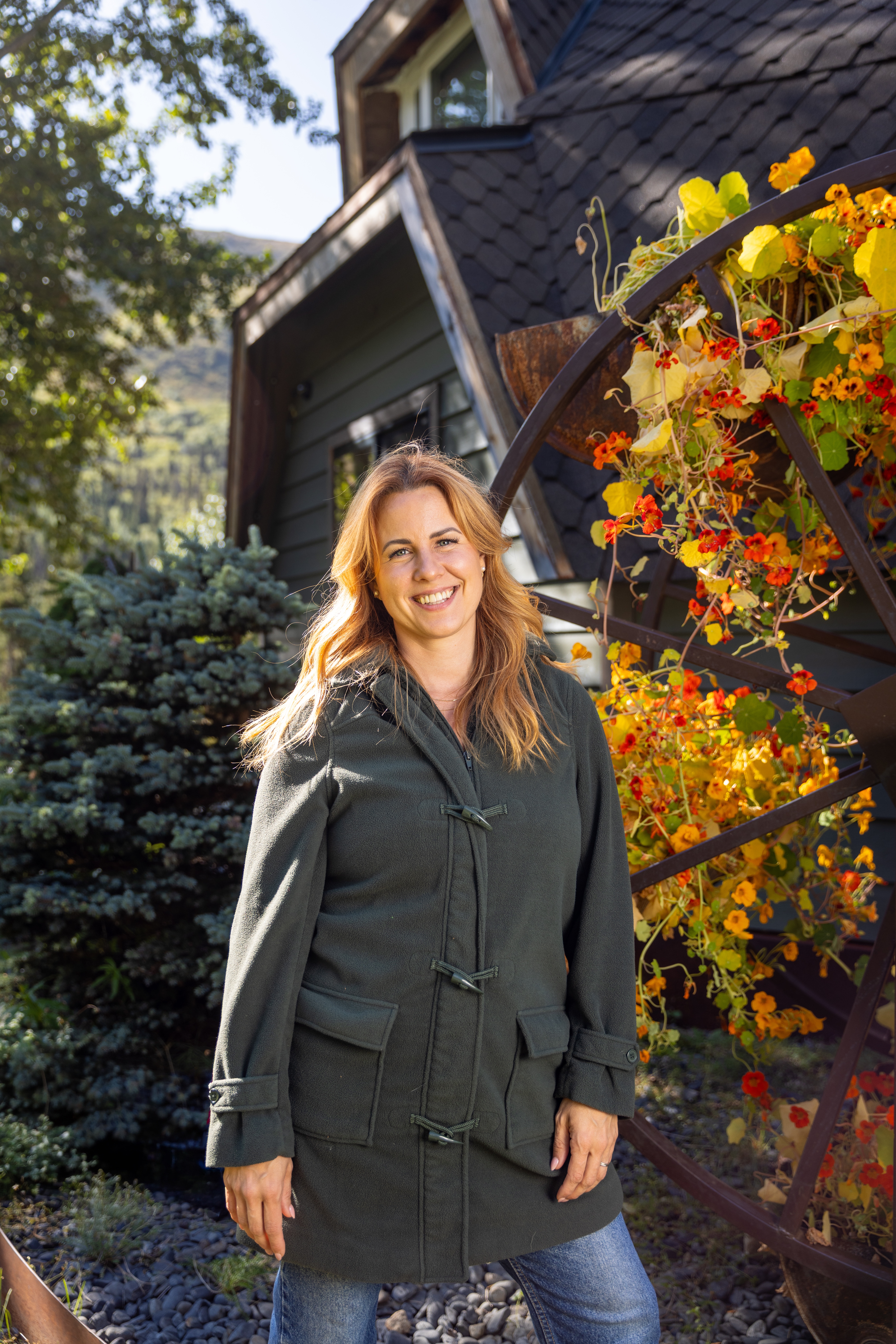 Ruby Jones in an olive coat smiling near a flowering trellis