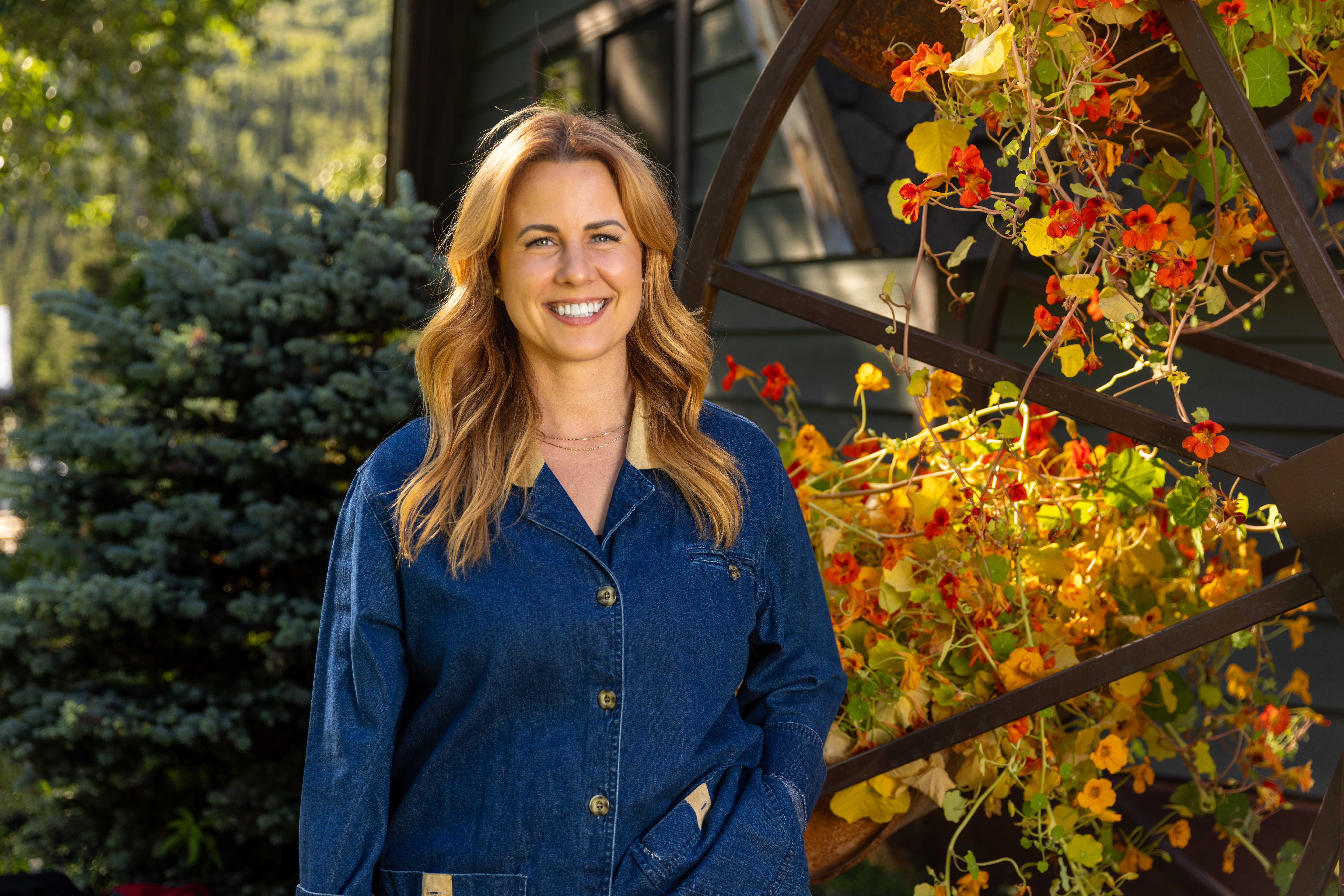 Ruby Jones in a denim shirt smiling near a flowering trellis