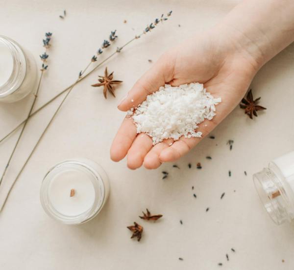 Flat lay of natural candle making with granulated wax, star anise, and lavender on a beige background.