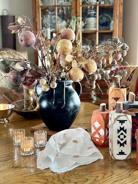 Southwestern style wood primitive pumpkins on a table with a pot filled with faux apple stems.