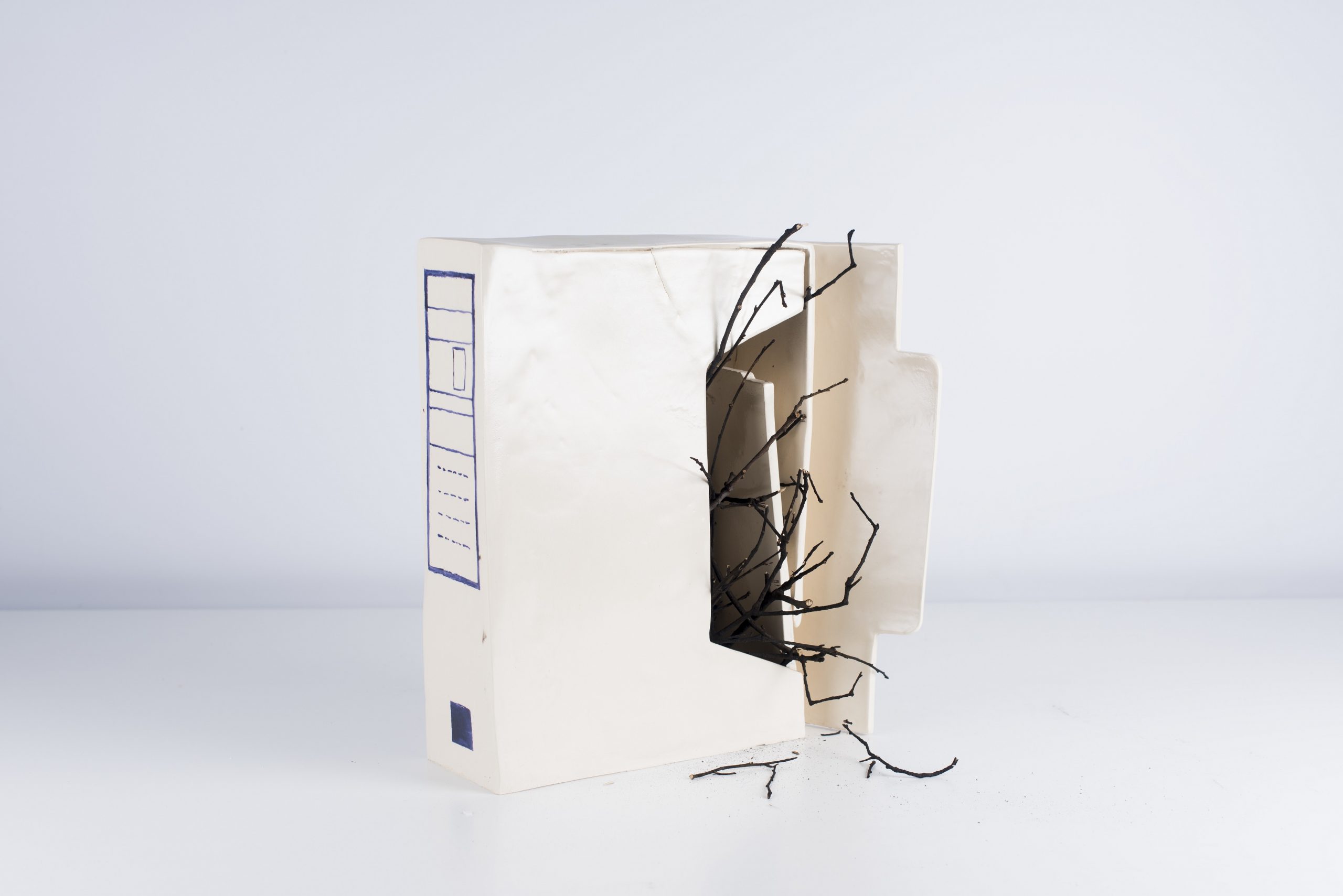 Descontrol programado: misma forma de carpeta archivadora en cerámica, con ramas quemadas y ennegrecidas atravesándola