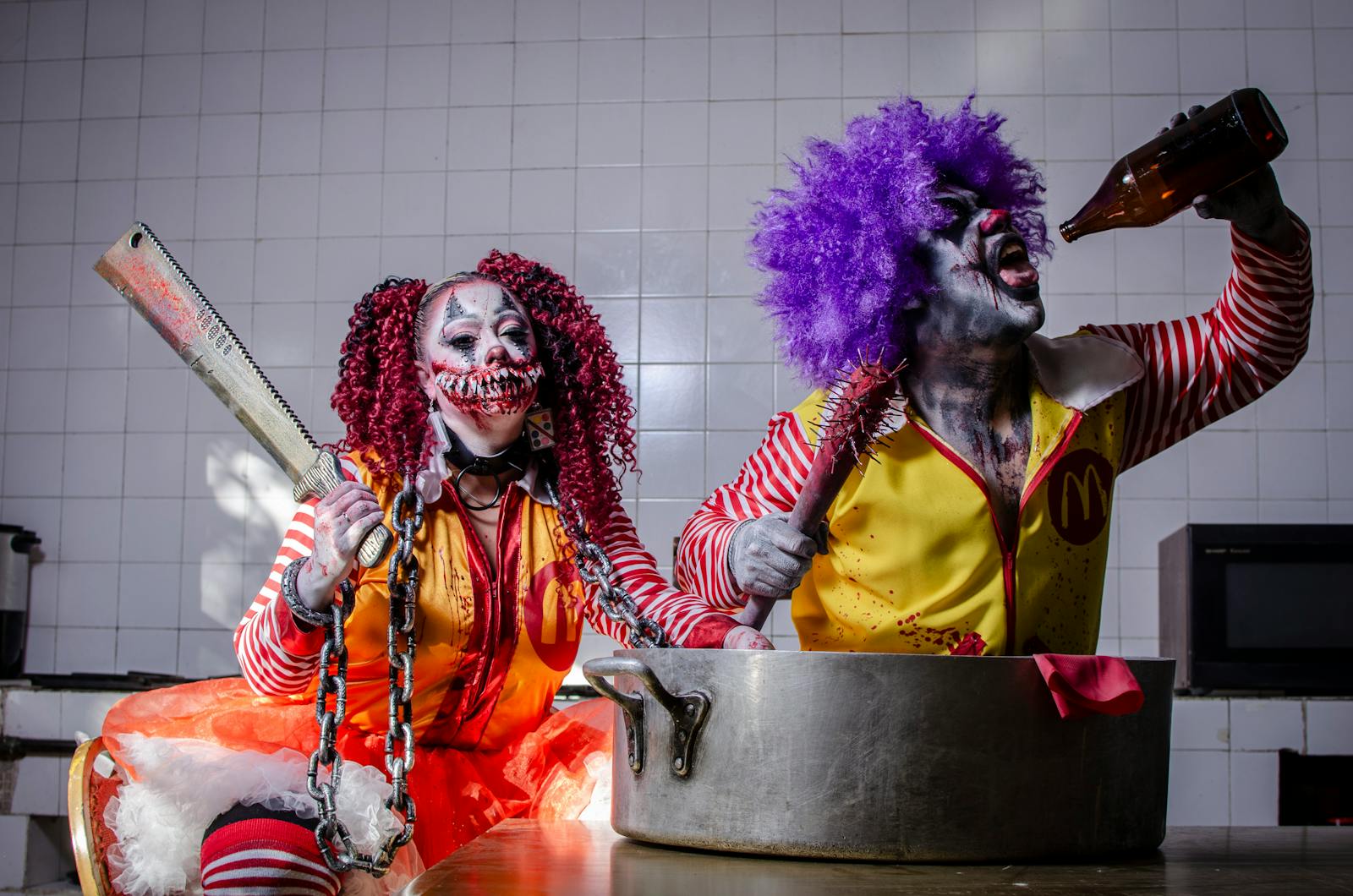 Two creepy clowns in a kitchen, one drinking, one with a chainsaw. Spooky and surreal.
