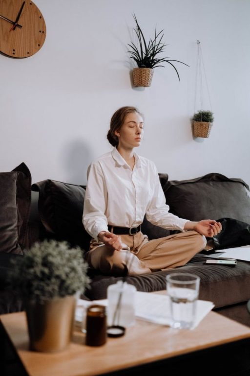 woman in white button up long sleeve shirt sitting on black couch in lotus position Meditation