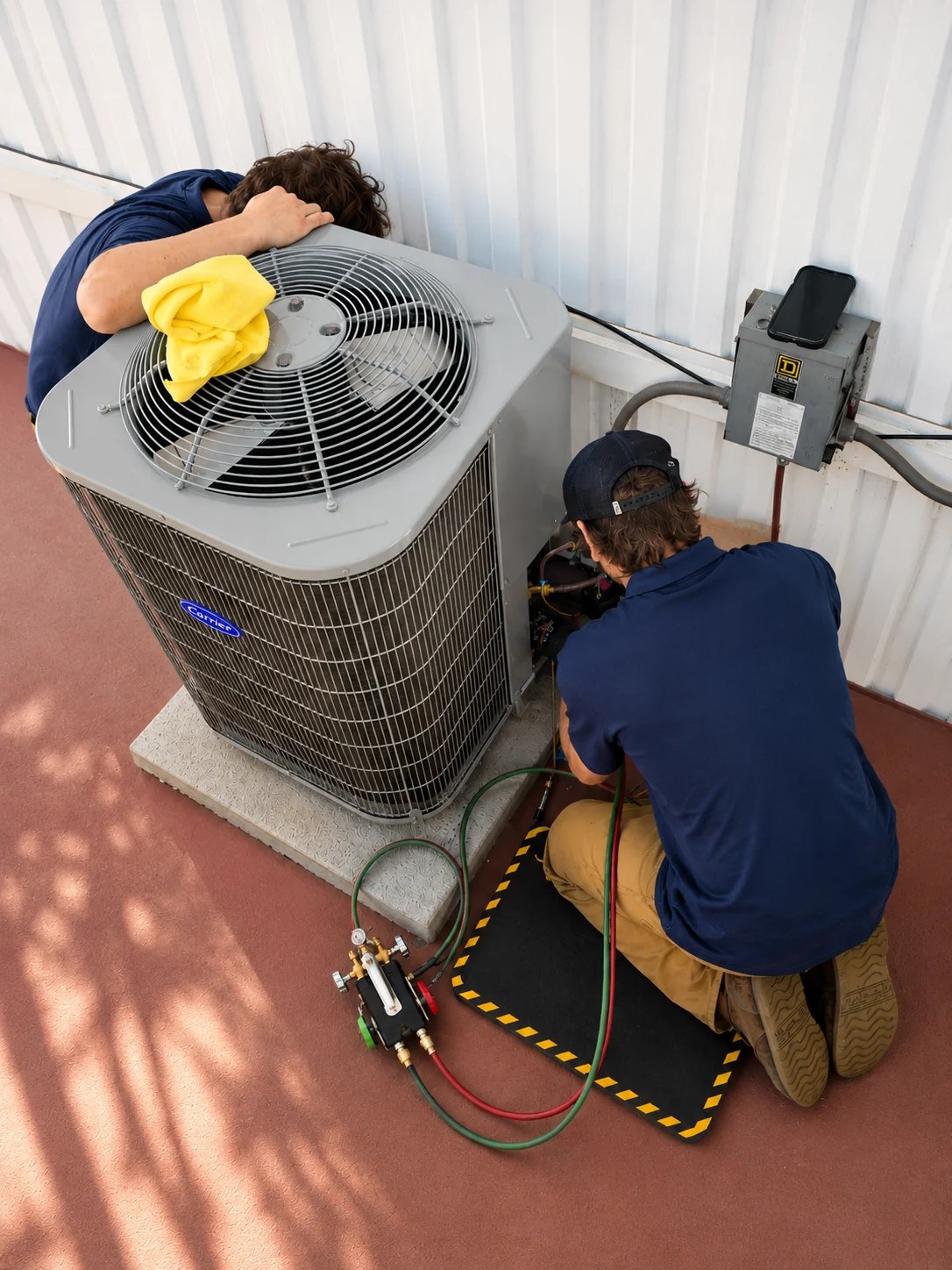 Two HVAC technicians servicing a Carrier outdoor air conditioning unit