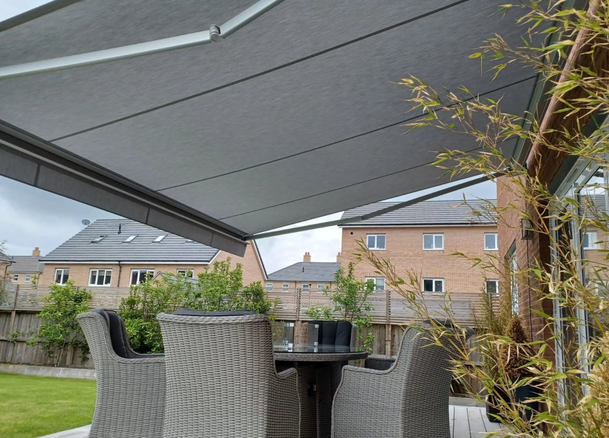 Quendon awning with grey fabric shading a rattan dining set on a garden patio
