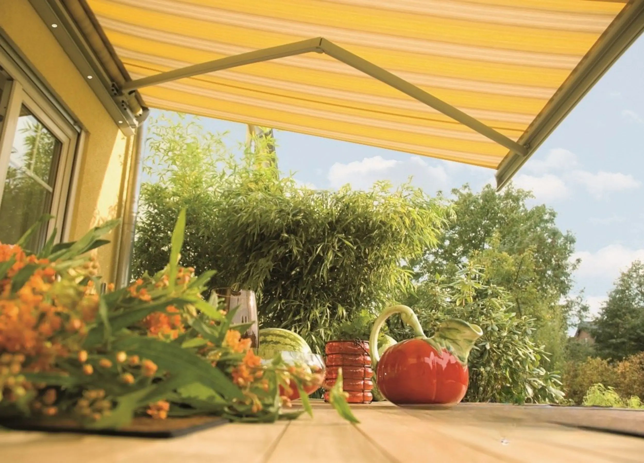 Weinor Semina awning extended with yellow striped fabric providing shade over garden patio.