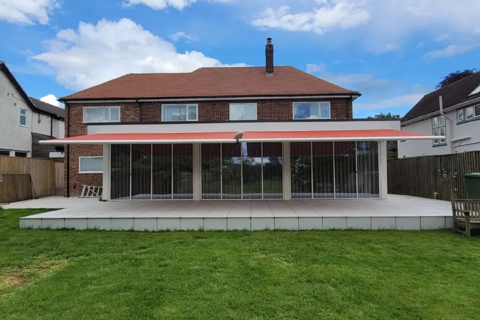Dual Weinor Cassita II awnings in red extended over glass veranda on a modern brick home
