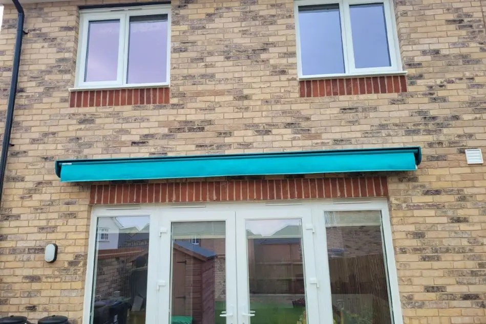 Weinor Topas awning installed in Ely with turquoise fabric on brick home