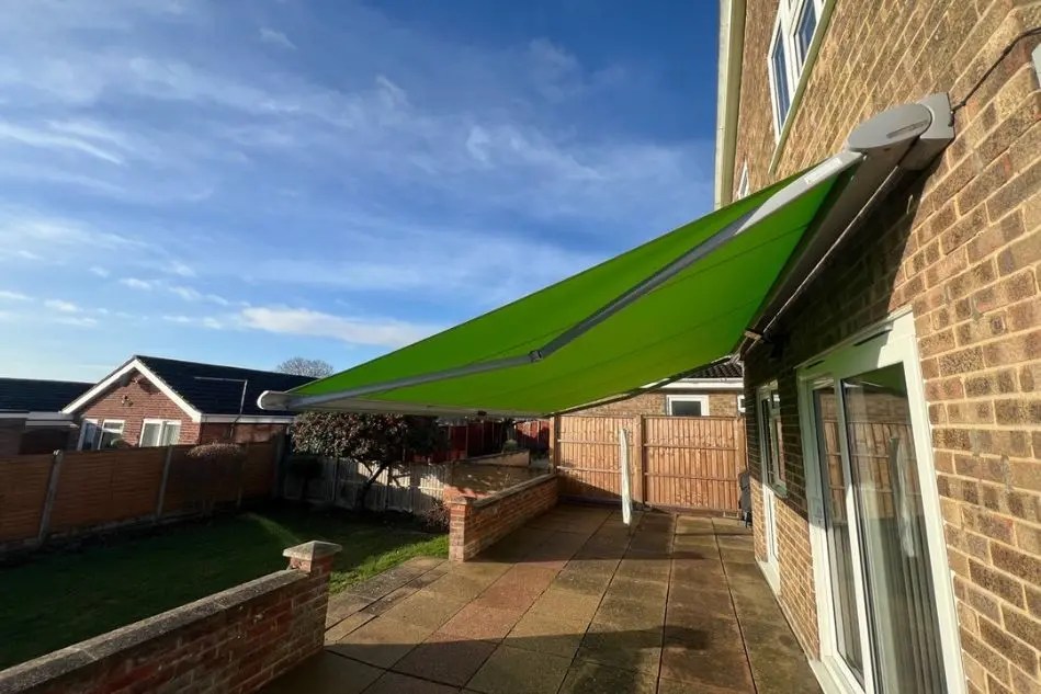 Green retractable awning installed on brick house patio providing shade