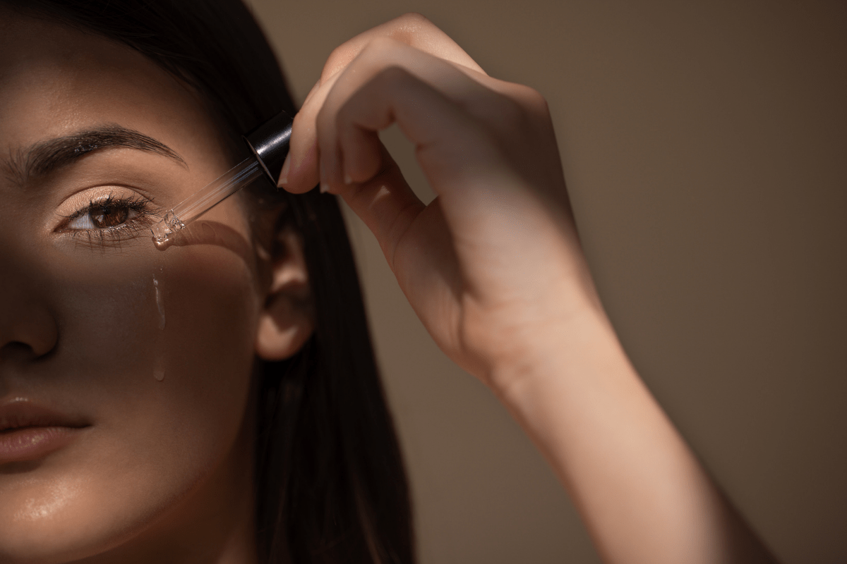 A close-up of a woman applying a hydrating face serum with a dropper, demonstrating daily skincare routine essentials for glowing skin.