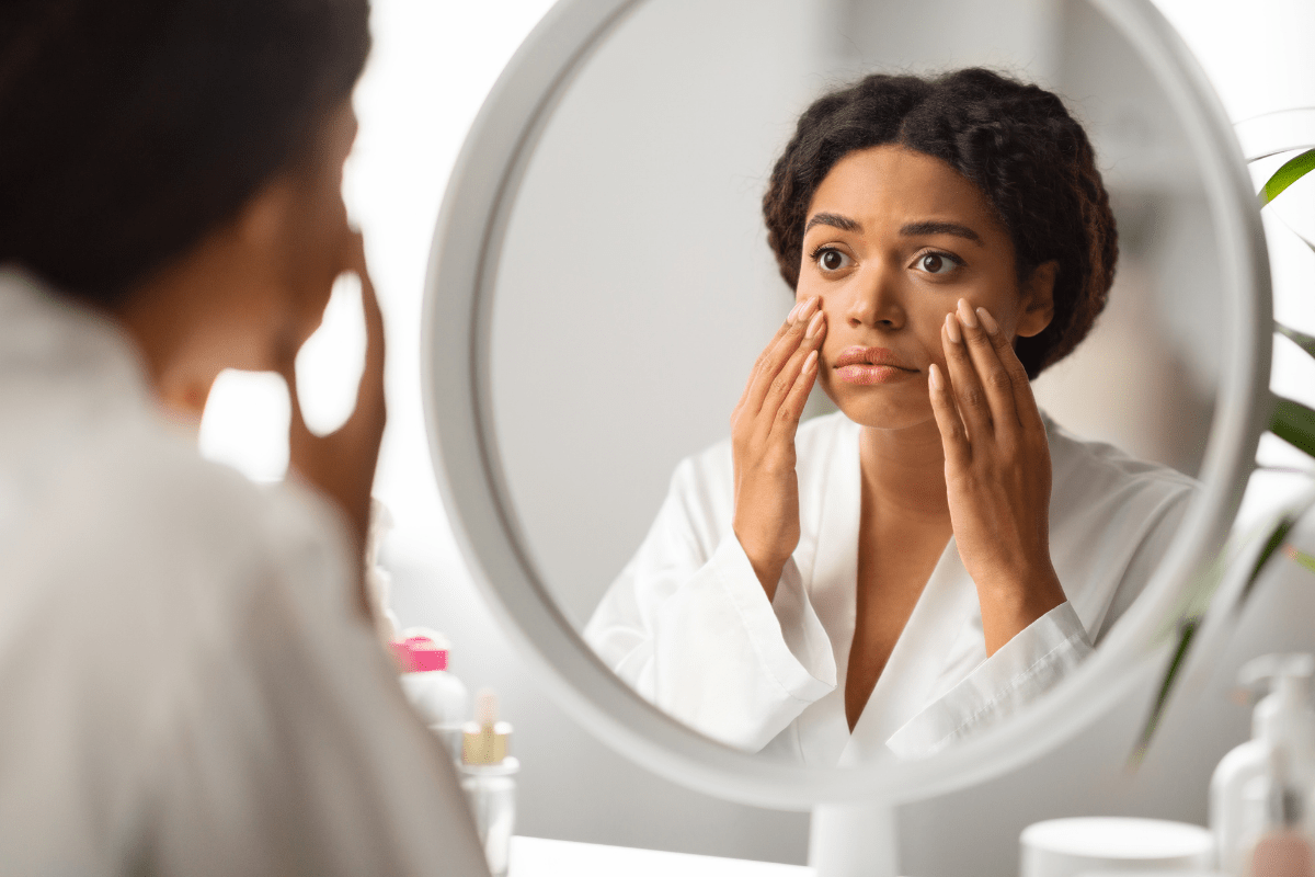 A woman examining her face in a round mirror, illustrating the differences between physical exfoliation and advanced skin-smoothing treatments.